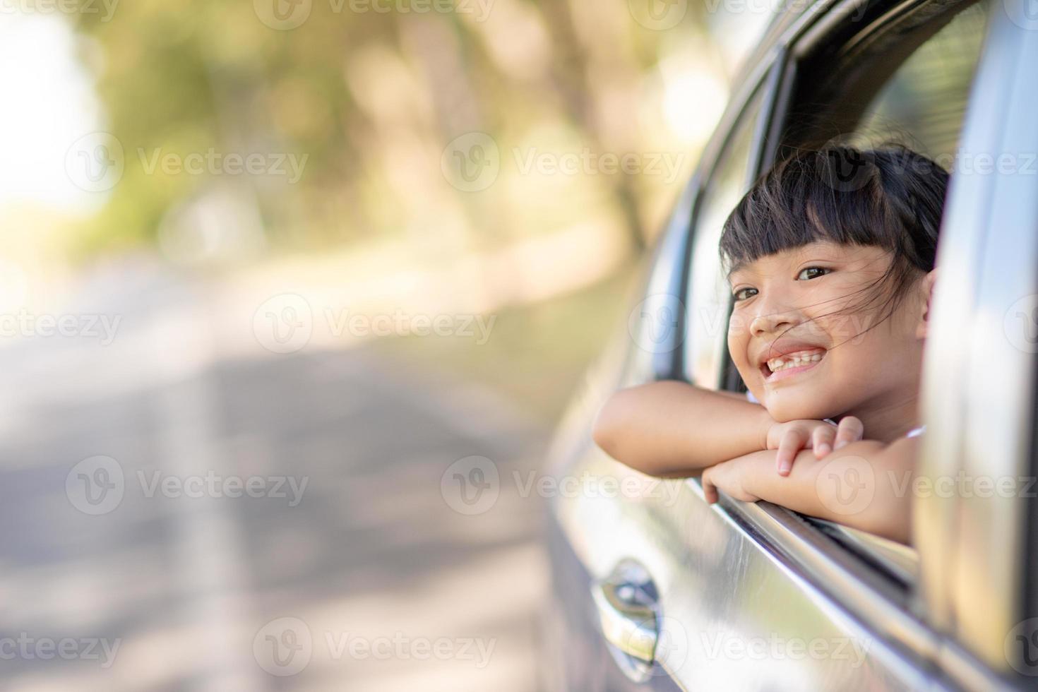 Cute asian little child girl having fun to travel by car and looking out from ar window in cthe countryside photo