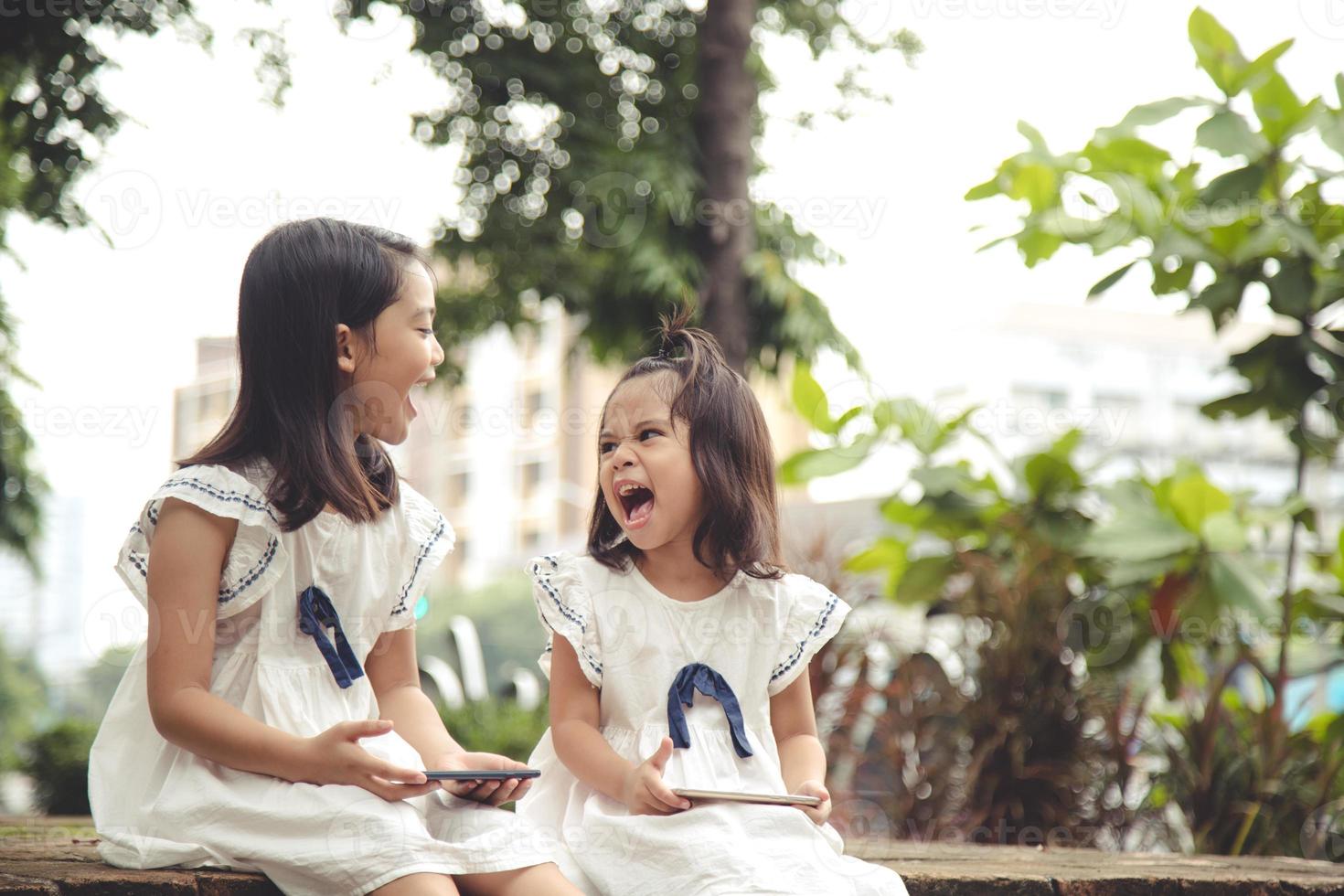 concepto de niños y artilugios. dos niñas hermanos hermanas miran el teléfono y sonríen. sostienen un teléfono inteligente, ven videos, aprenden, juegan, hablan en línea. Internet para niños. control parental foto