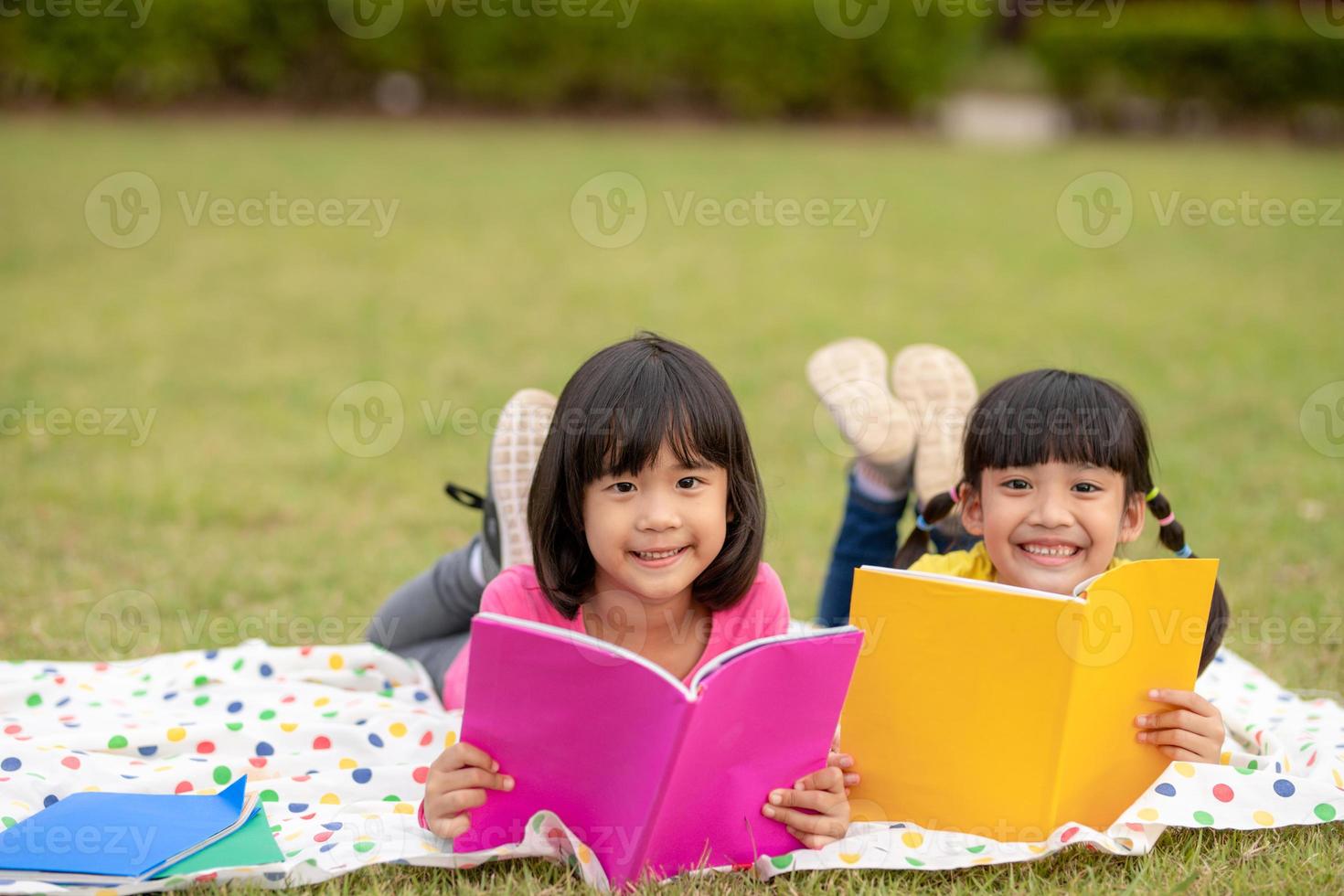 dos hermosas niñas leyendo libros en el jardín, sentadas en el césped. el concepto de educación y amistad. foto