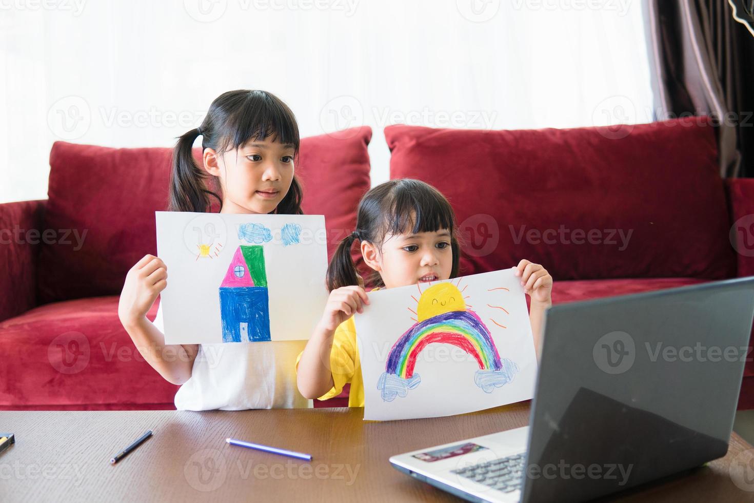 Two asian child girl students study online with teacher by video call together. Siblings are homeschooling with computer laptop during quarantine due to Covid 19 pandemic. photo