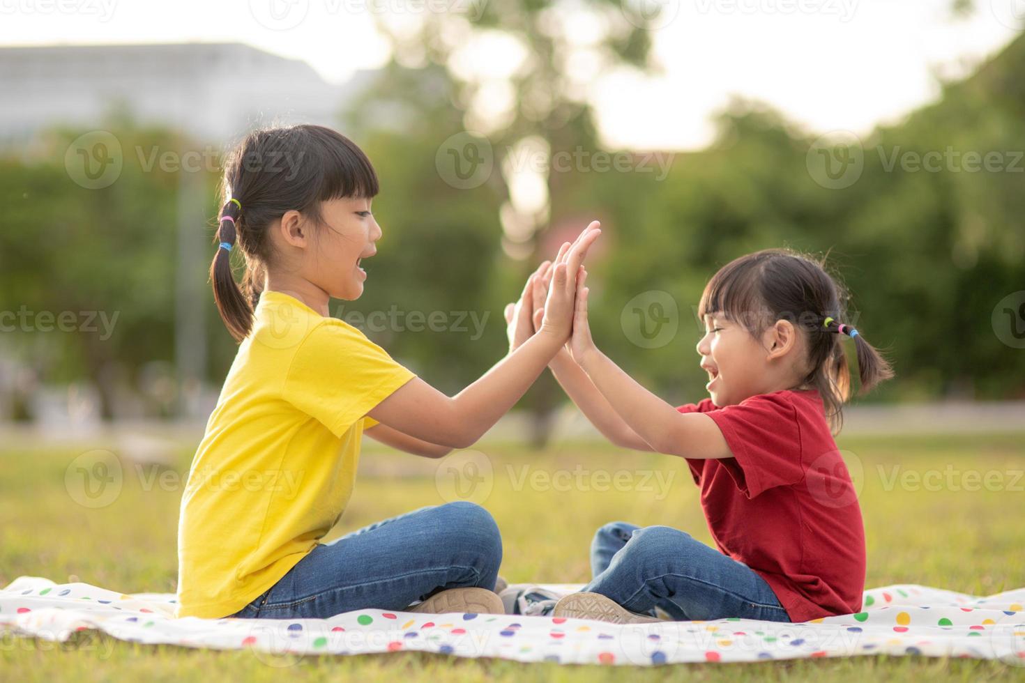 Two little girls sitting on the grass in the park and playing rock paper scissors hand game photo