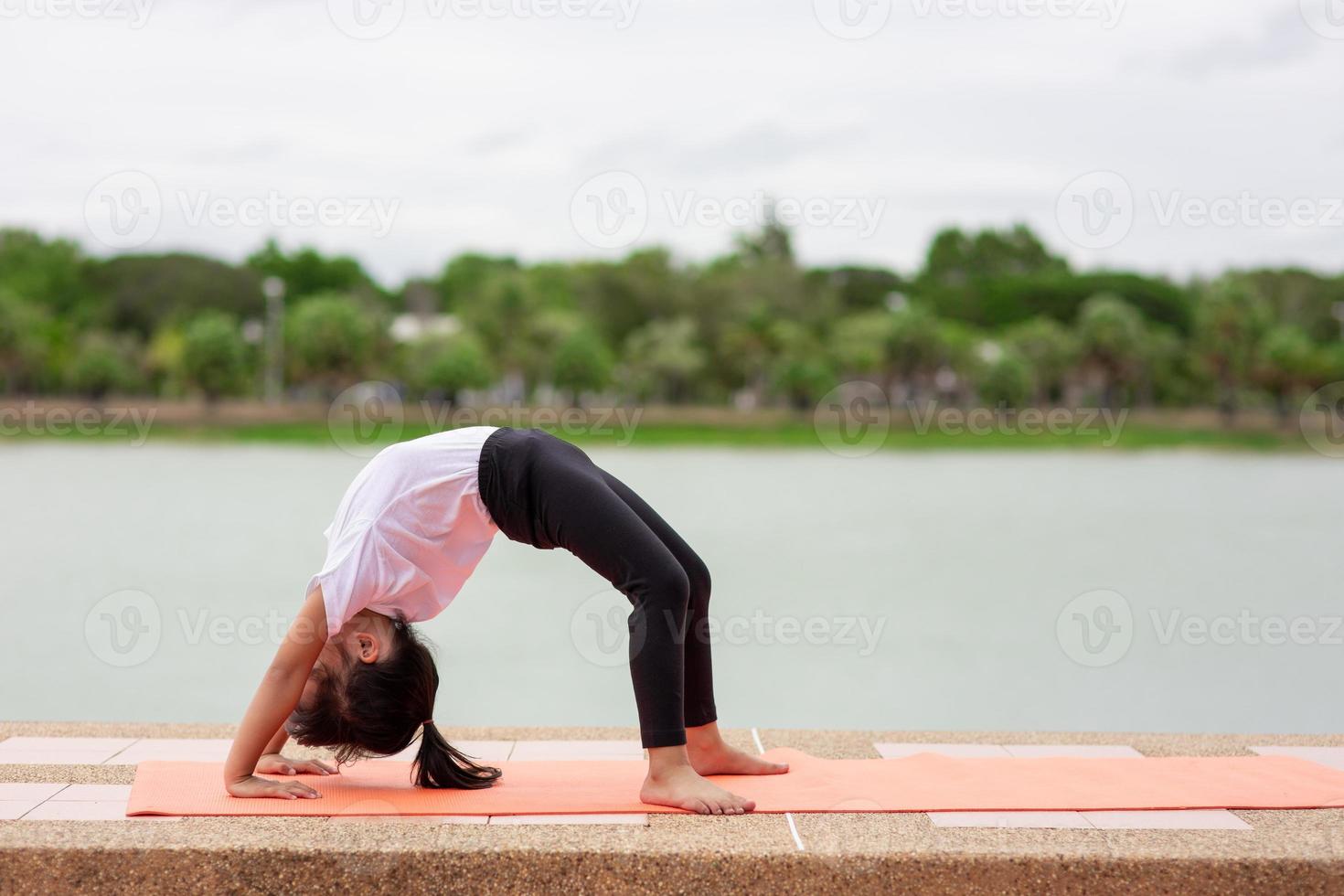 pequeña y linda niña asiática practicando pose de yoga en una alfombra en el parque, concepto saludable y de ejercicio foto