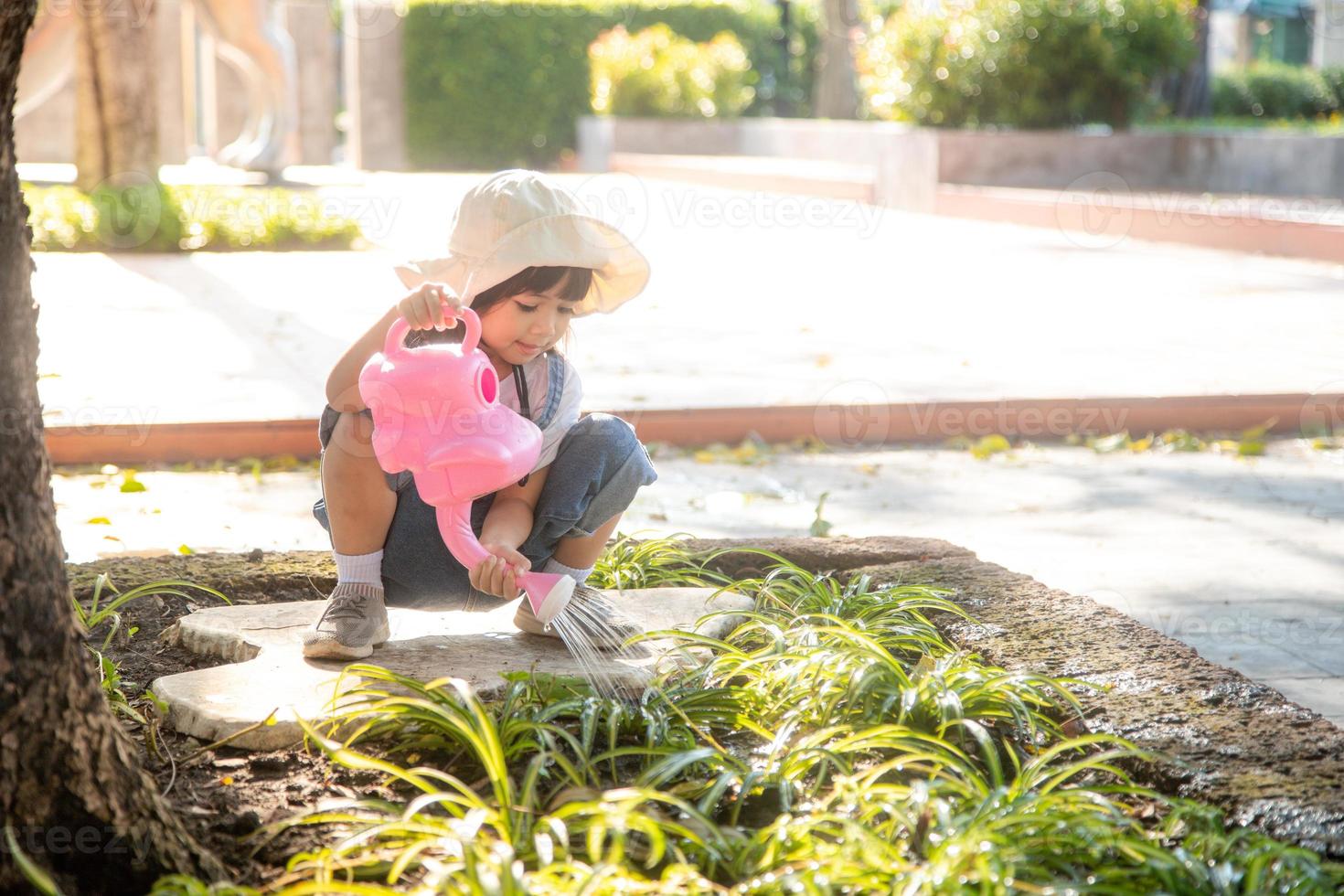 niña asiática vertiendo agua en los árboles. niño ayuda a cuidar las plantas con una regadera en el jardín. foto