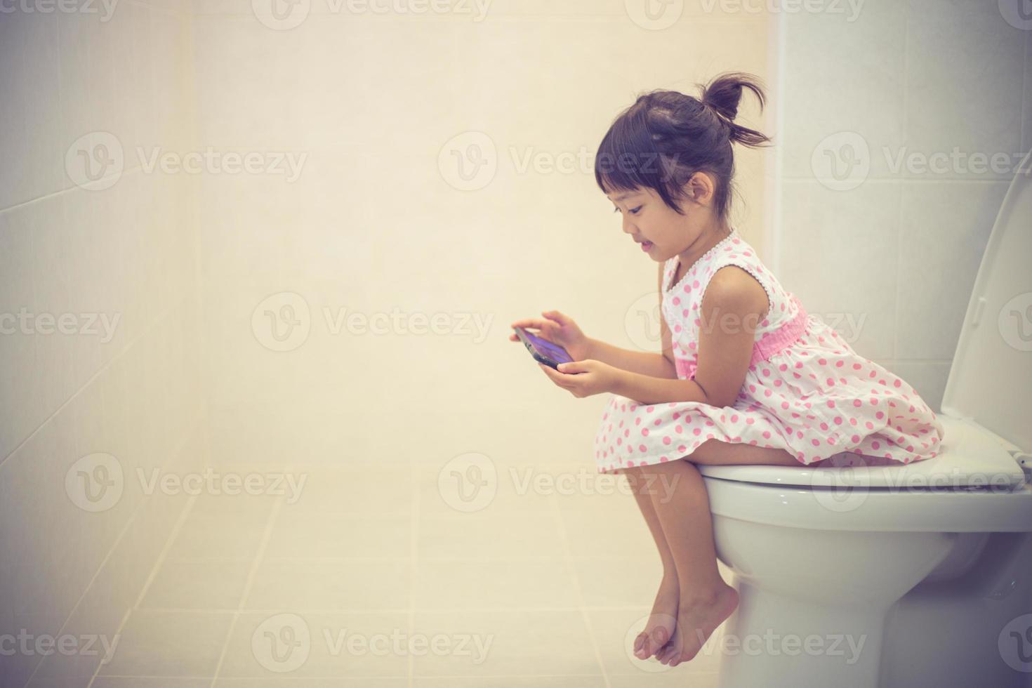 asian children sitting on a toilet and holding smartphone. photo