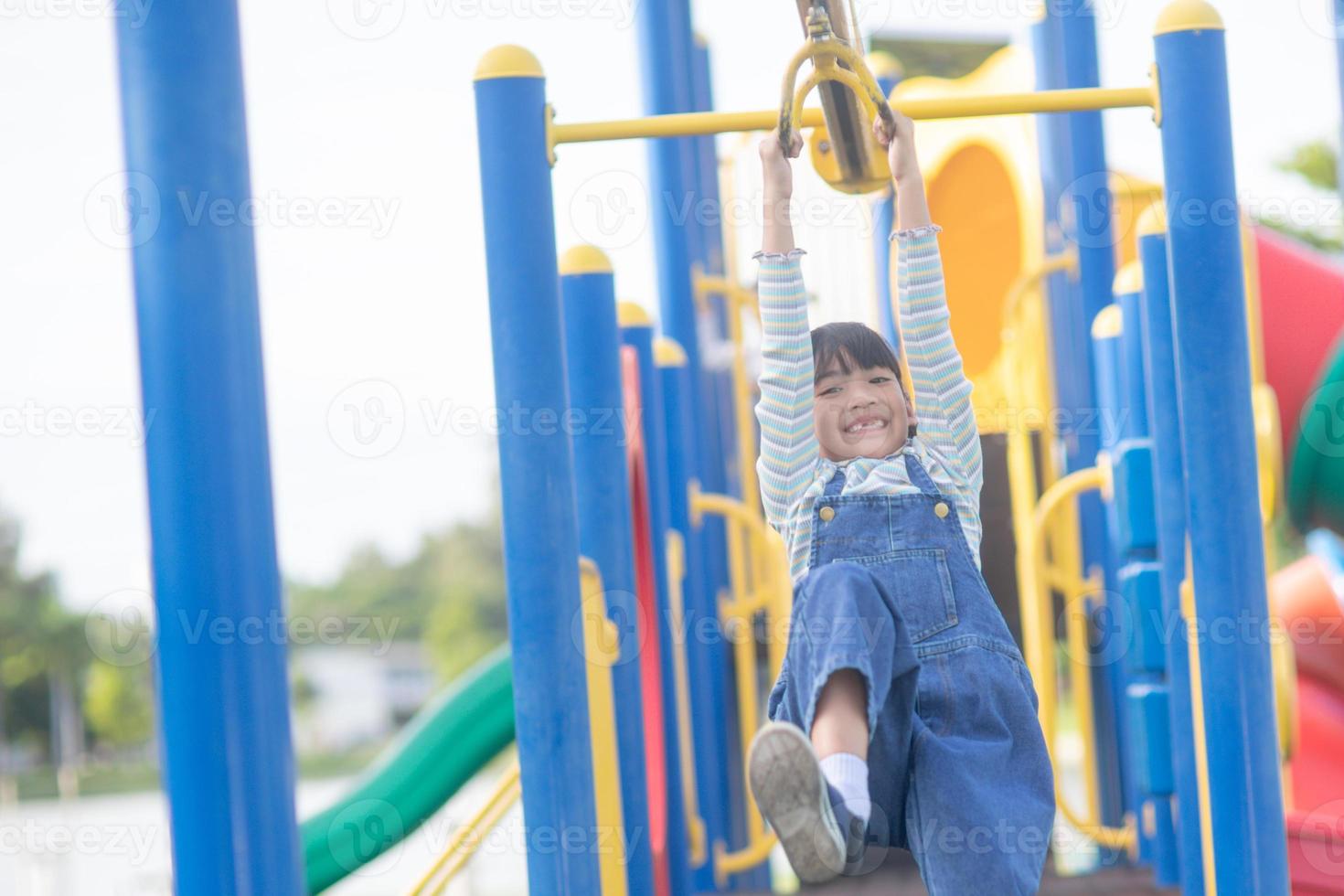 A little girl in casual clothes playing on kids playground, holding and climbing. Selective focus on girl's head. photo