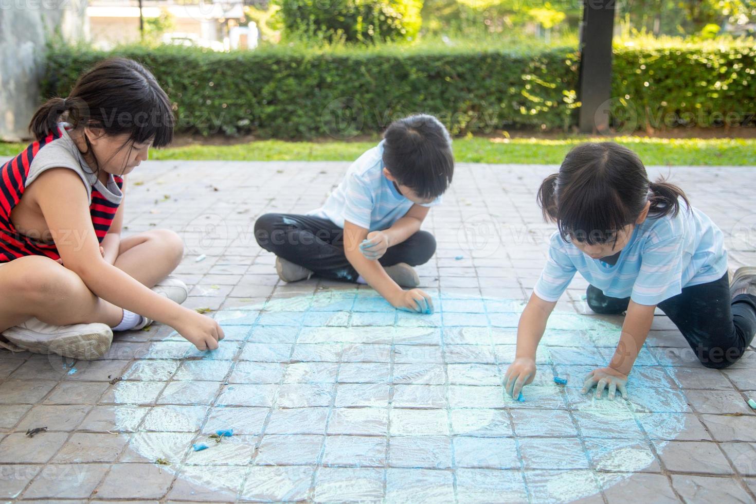 Asian children play outdoors. Child girl draws a planet globe with a map of the world colored chalk on the pavement, asphalt. Earth, peace day concert. photo