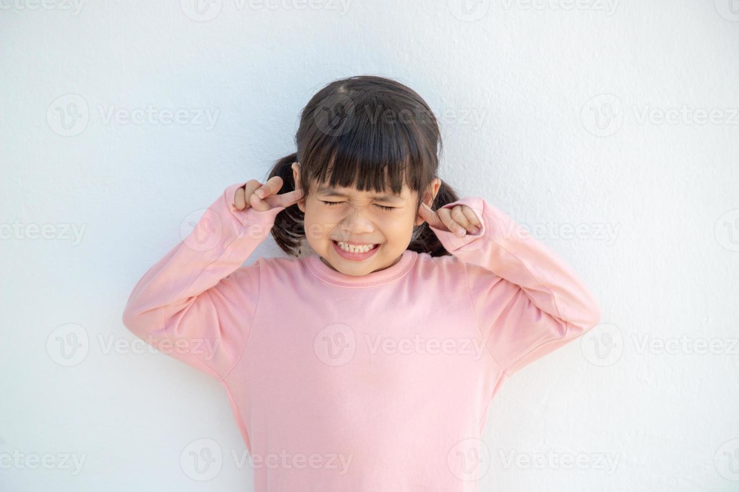 una linda niña asiática cubrió las orejas con los dedos y hizo un gesto de que no quería escuchar en un fondo blanco con un espacio de copia vacío foto