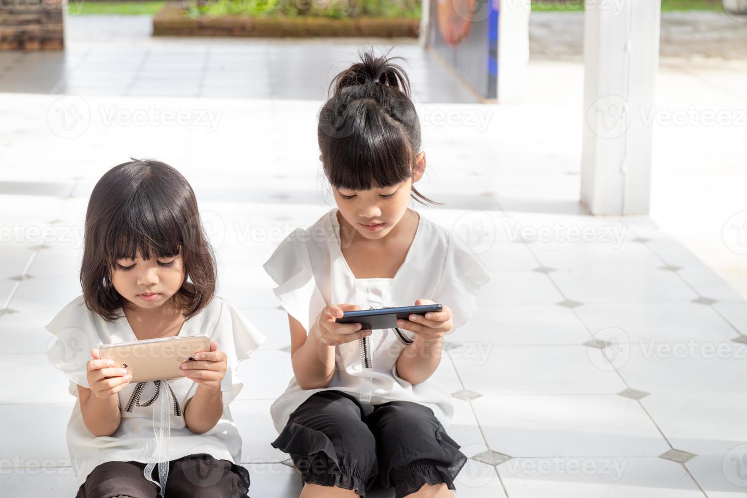 Sibling girls watching their smartphones on white background. Social concept about new technology people addiction photo