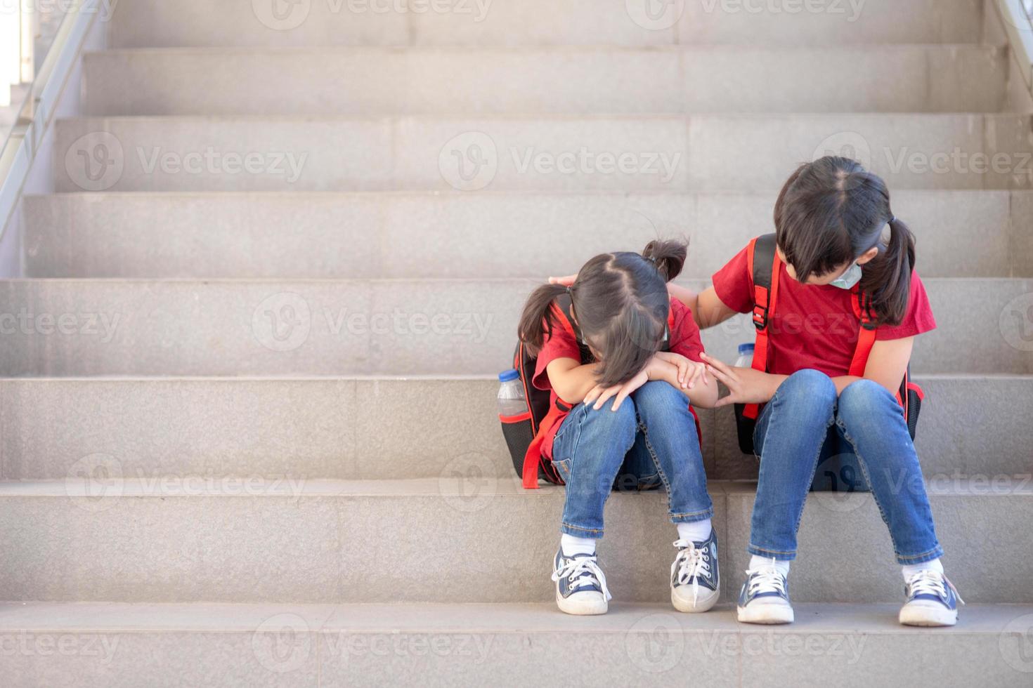 retrato de una colegiala llorando mientras se sienta en las escaleras al aire libre con una hermana sonriente consolándola, copiando espacio foto