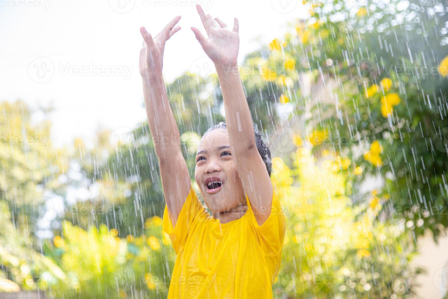 niña asiática feliz divirtiéndose para jugar con la lluvia a la luz del sol foto