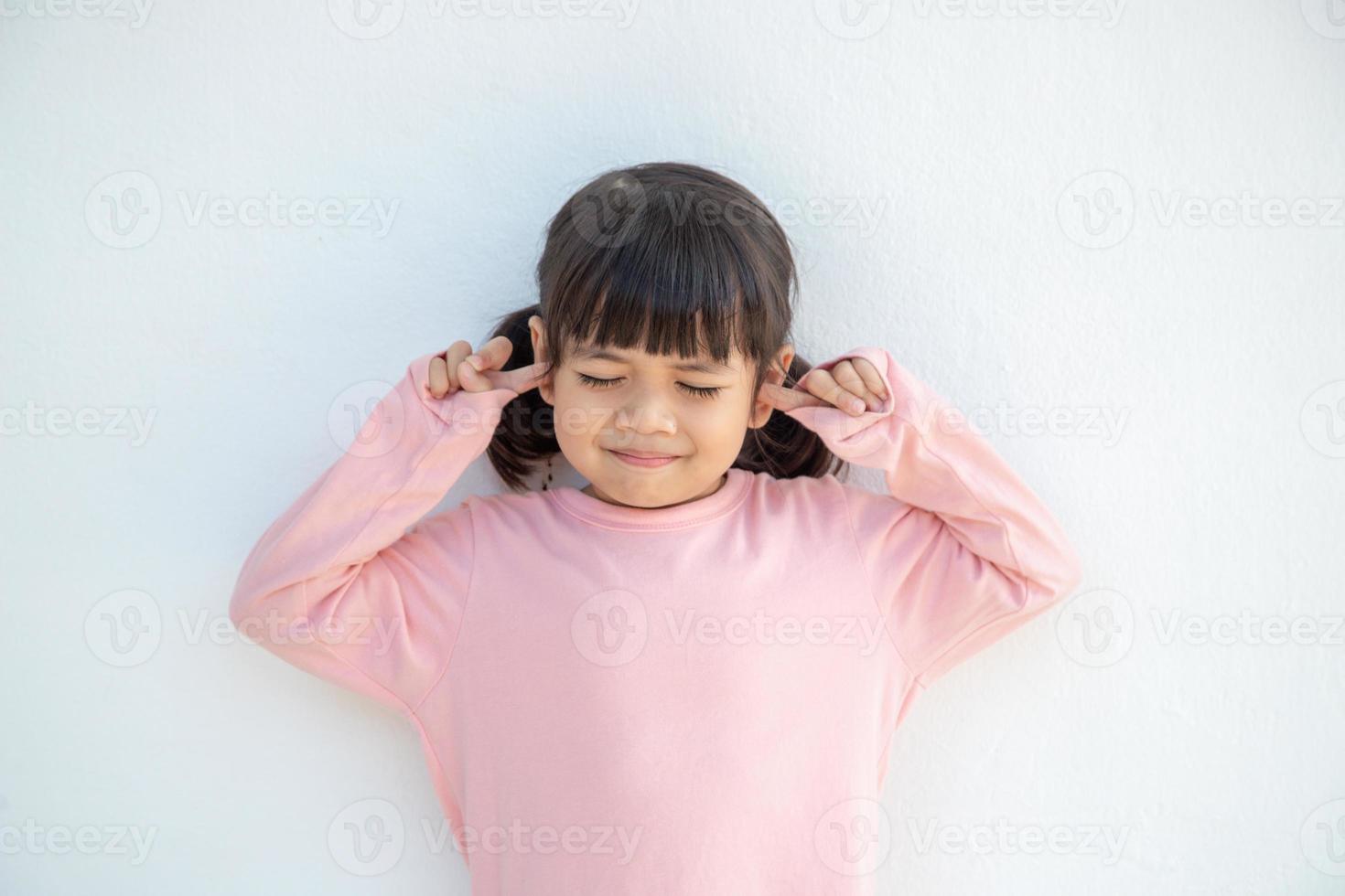 una linda niña asiática cubrió las orejas con los dedos y hizo un gesto de que no quería escuchar en un fondo blanco con un espacio de copia vacío foto