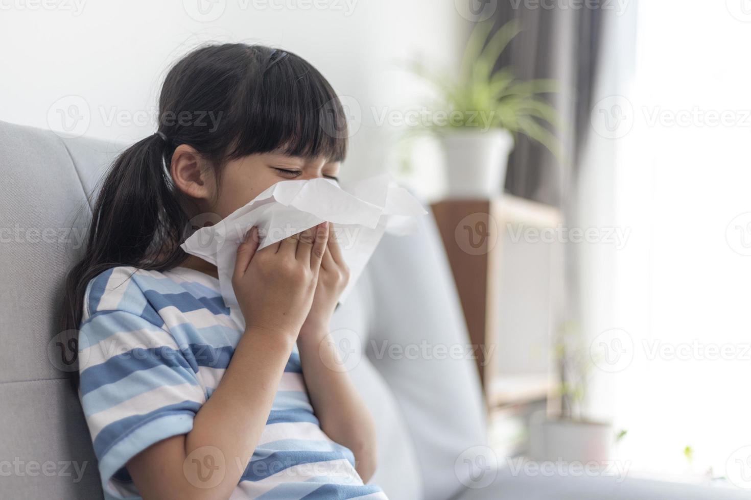 Unhealthy kid blowing nose into tissue, Child suffering from running nose or sneezing, A girl catches a cold when season change, childhood wiping nose with tissue photo