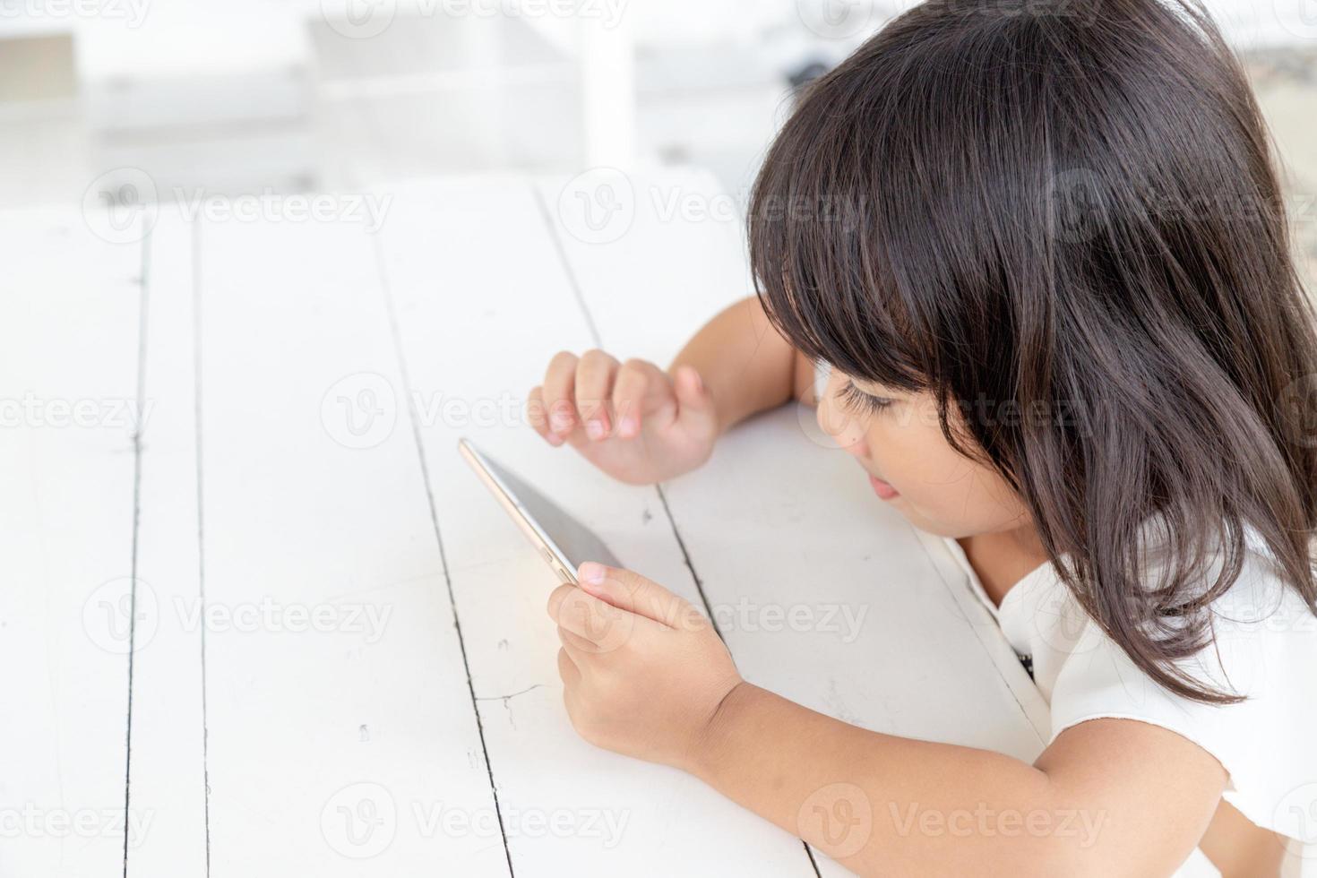 Asian girl playing smartphone on the table. watching smartphone. Kids use phones and play games. child use mobile. addicting game and cartoon photo