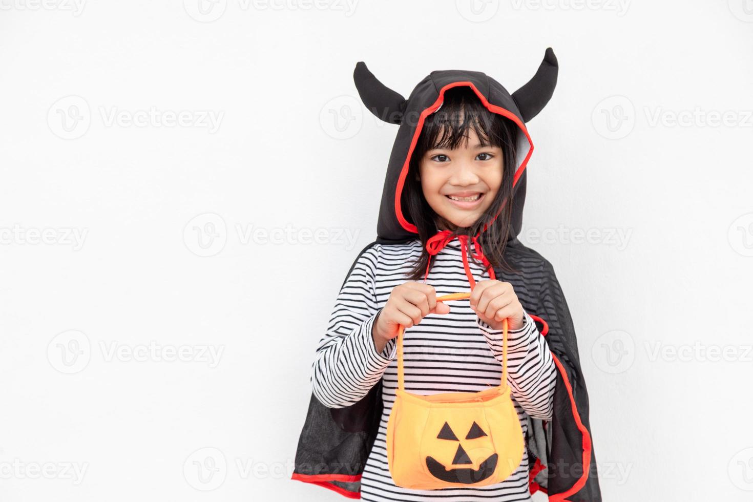 divertido concepto de niño de halloween, niña linda con disfraz de fantasma de halloween aterrador que sostiene un fantasma de calabaza naranja en la mano, sobre fondo blanco foto