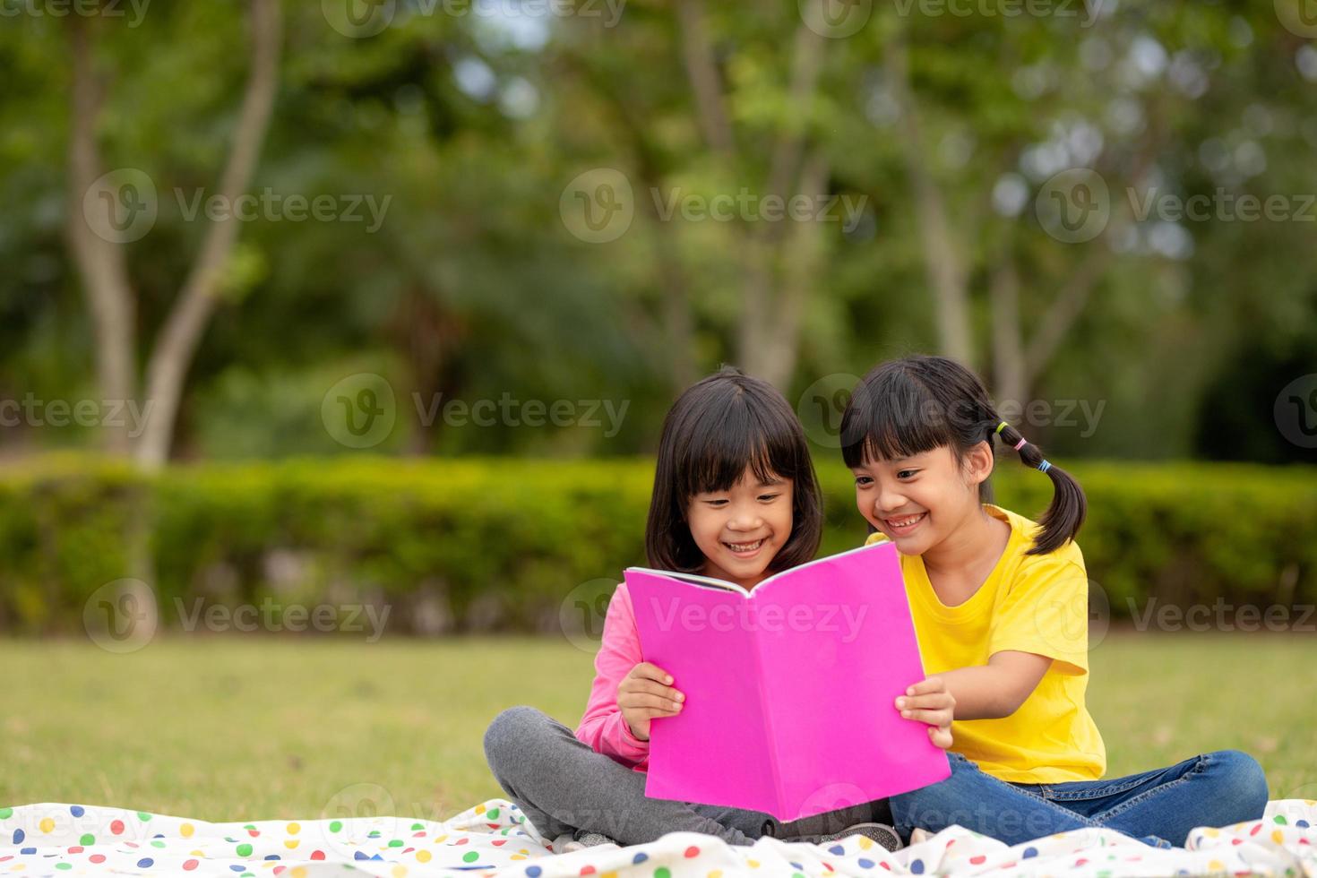 two beautiful little girls reading books in the garden , sitting on grass. The concept of education and friendship. photo