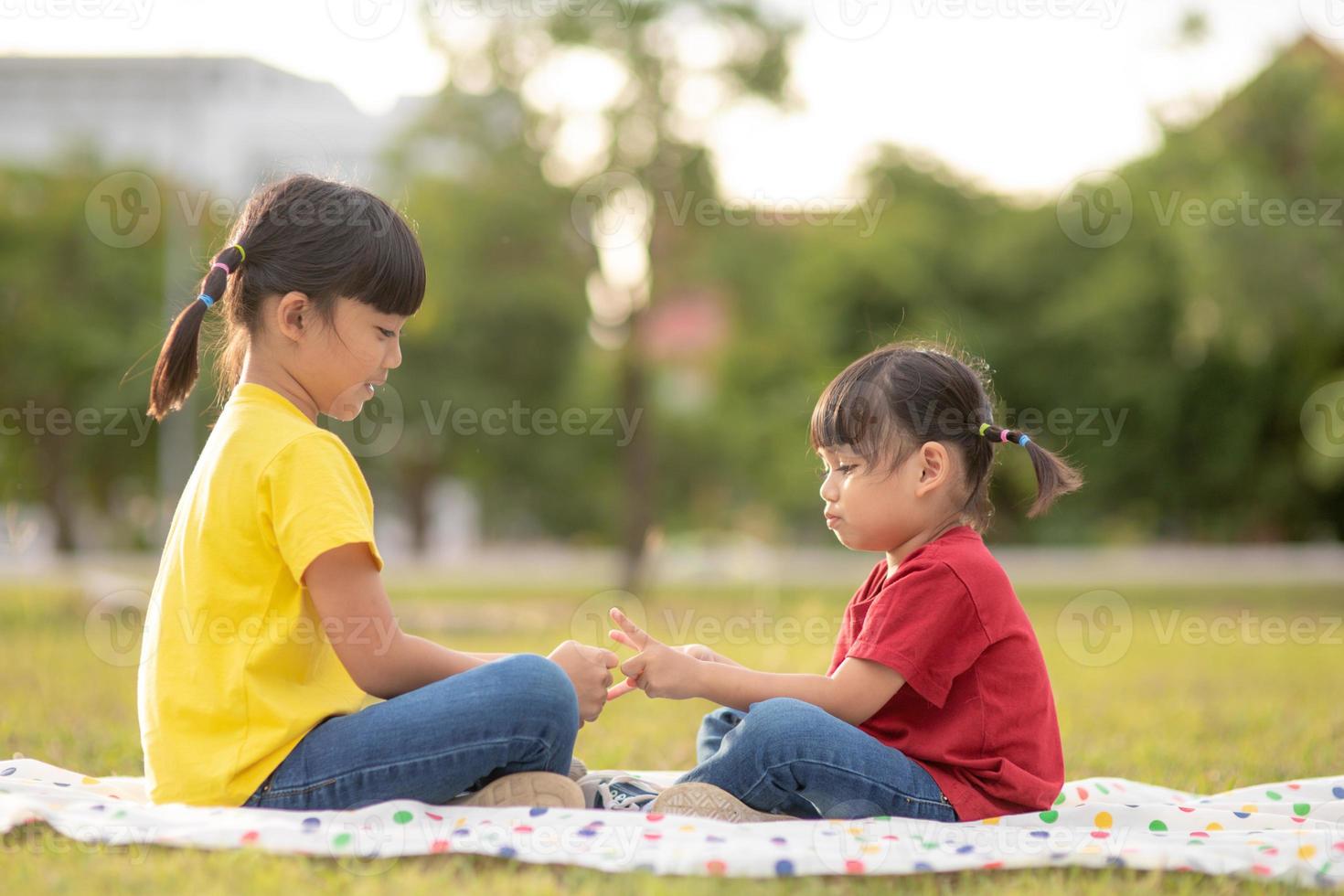 Two little girls sitting on the grass in the park and playing rock paper scissors hand game photo