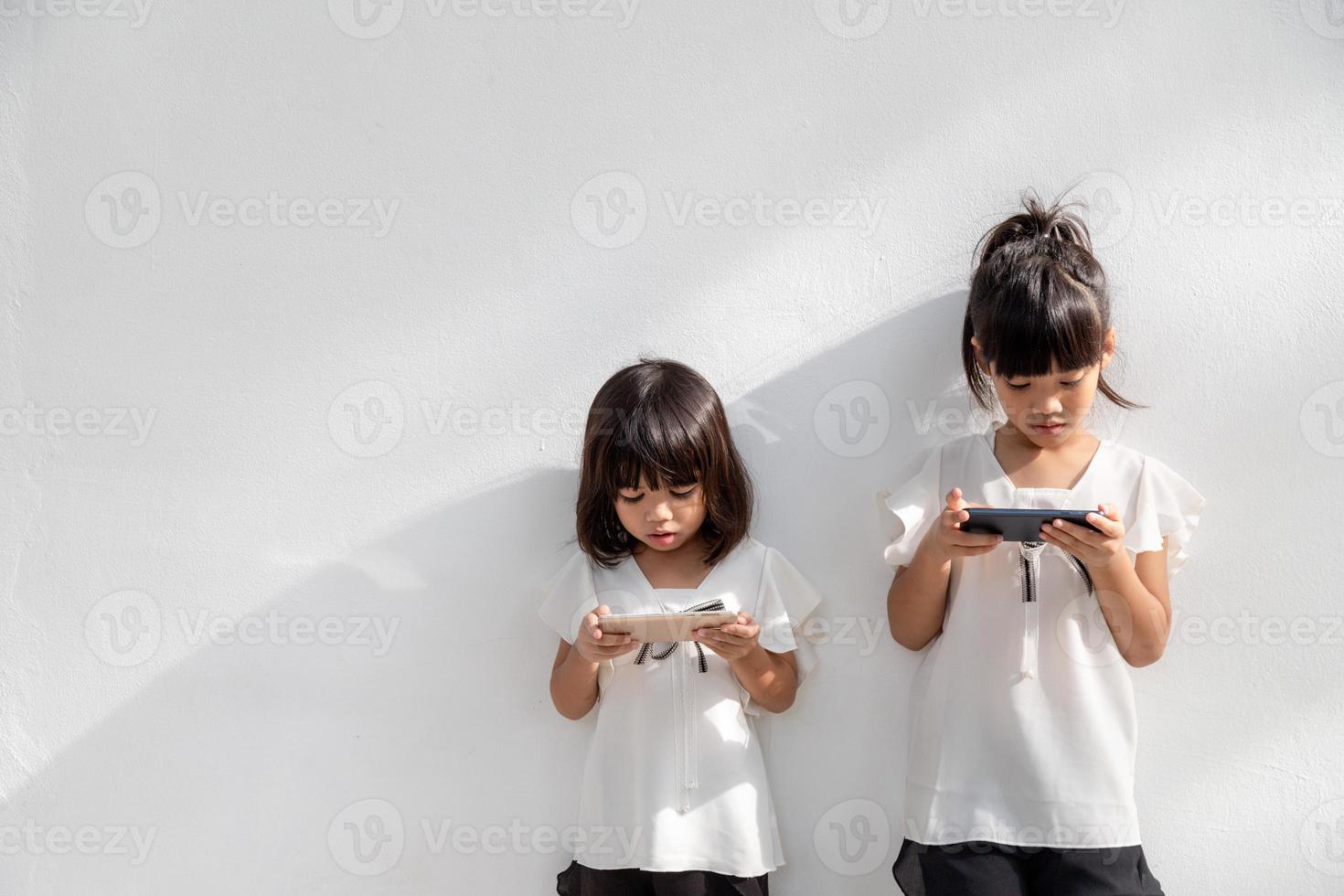 Sibling girls watching their smartphones on white background. Social concept about new technology people addiction photo