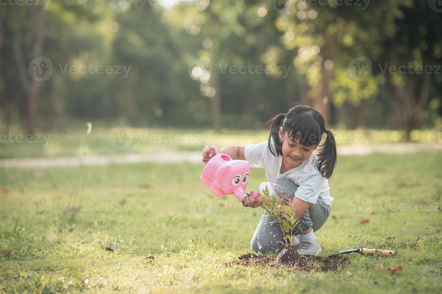 niña asiática vertiendo agua en los árboles. niño ayuda a cuidar las plantas con una regadera en el jardín. foto