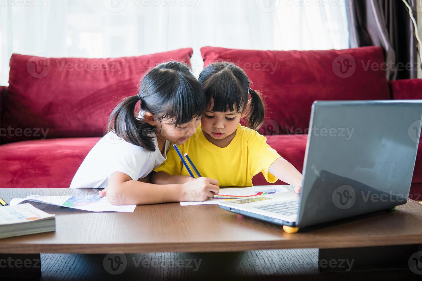 Two asian child girl students study online with teacher by video call together. Siblings are homeschooling with computer laptop during quarantine due to Covid 19 pandemic. photo