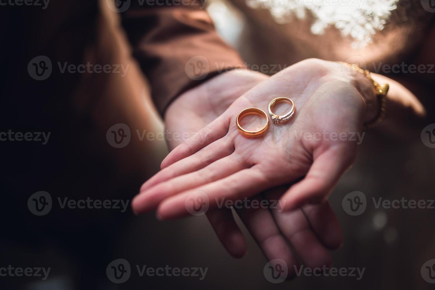 Closeup photo of bride and groom holding golden wedding rings on hands - Image