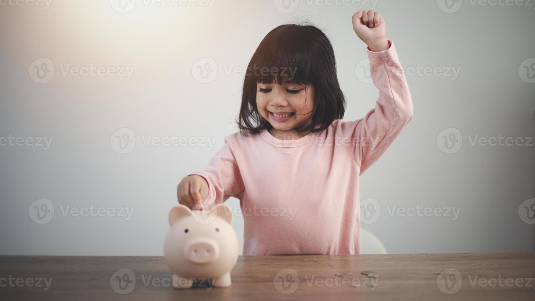 Little Asian girl saving money in a piggy bank, learning about saving, Kid save money for future education. Money, finances, insurance, and people concept photo