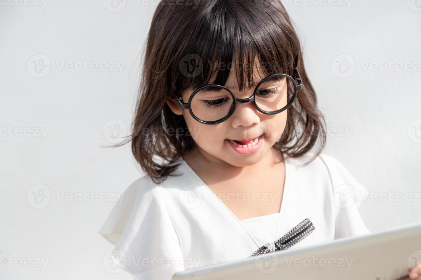 A little girl is concentrated on the tablet, look at the tablet, technology concept for children, profile view, isolated on white background, copy space photo