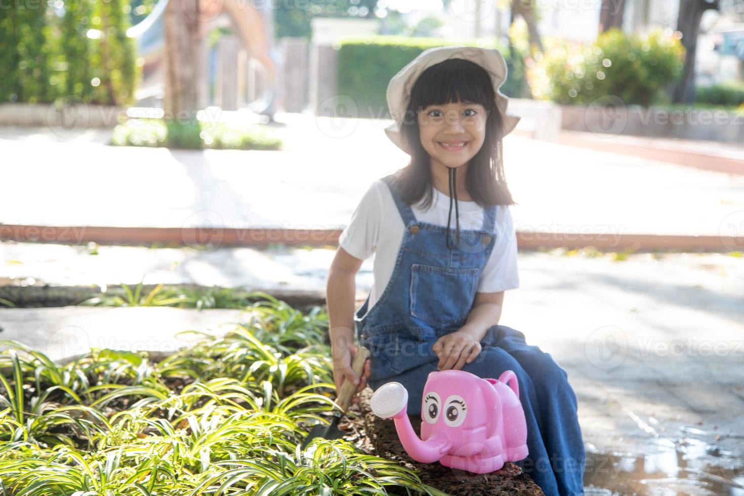 niña asiática vertiendo agua en los árboles. niño ayuda a cuidar las plantas con una regadera en el jardín. foto