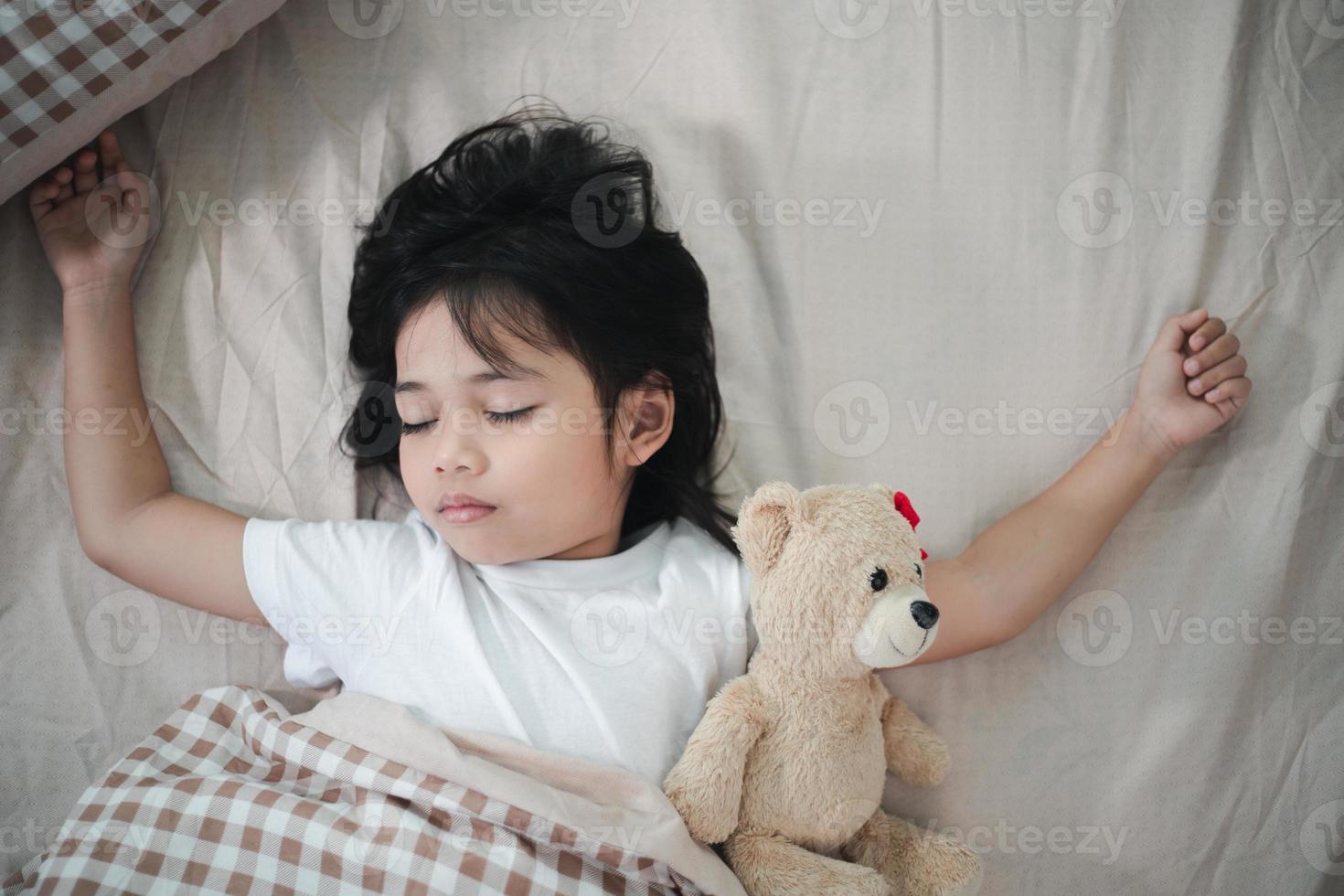 child little girl sleeps in the bed with a toy teddy bear photo