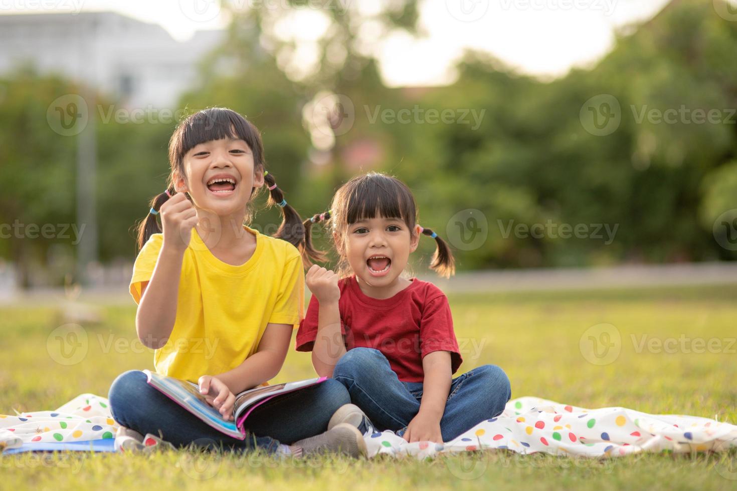 two beautiful little girls reading books in the garden , sitting on grass. The concept of education and friendship. photo