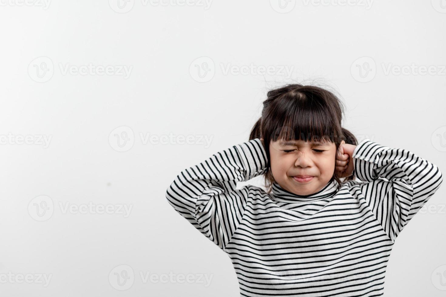 una linda niña asiática cubrió las orejas con los dedos y hizo un gesto de que no quería escuchar en un fondo blanco con un espacio de copia vacío foto