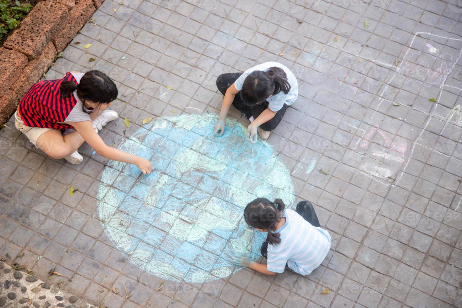 Asian children play outdoors. Child girl draws a planet globe with a map of the world colored chalk on the pavement, asphalt. Earth, peace day concert. photo