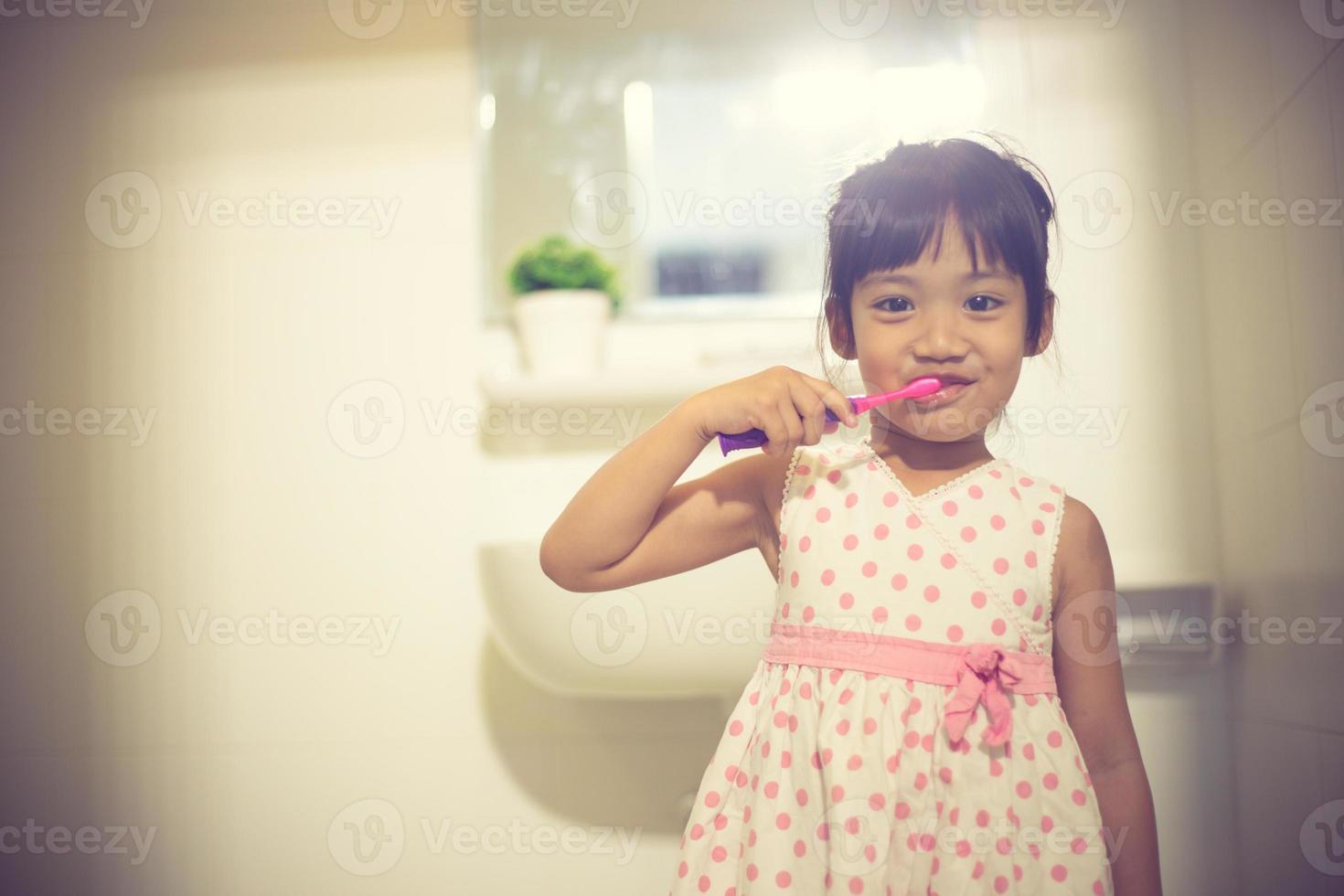 niñita linda limpiándose los dientes con cepillo de dientes en el baño foto