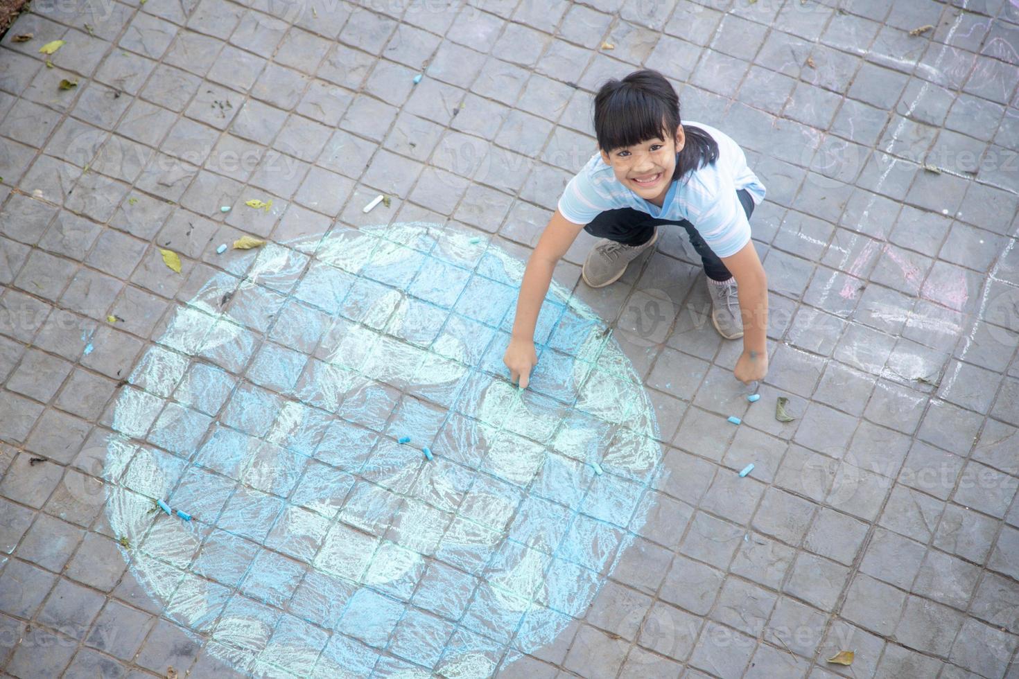 Asian children play outdoors. Child girl draws a planet globe with a map of the world colored chalk on the pavement, asphalt. Earth, peace day concert. photo