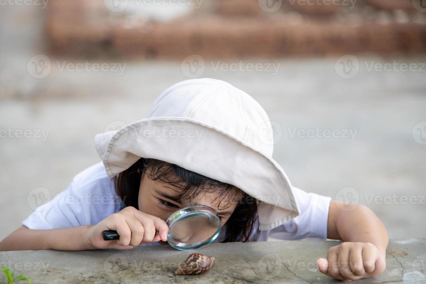 Happy kid girl exploring nature with a magnifying glass and a snail. He having fun in the garden. The concept of the kid is ready to go to school. photo
