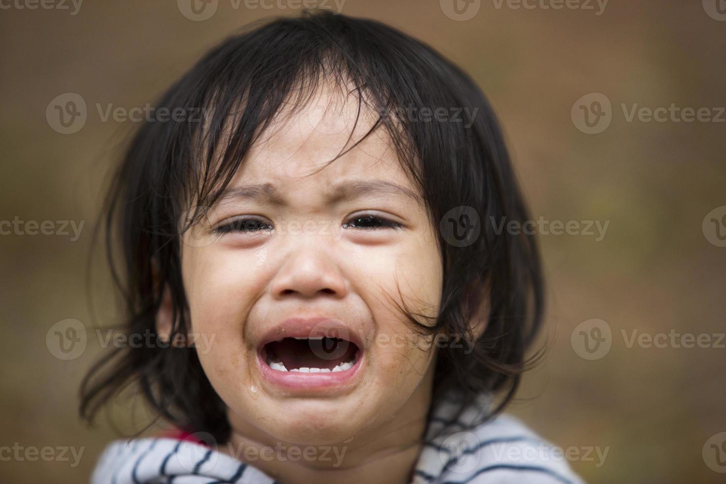 Cierra a una niña pequeña llorando con lágrimas en la cara. foto