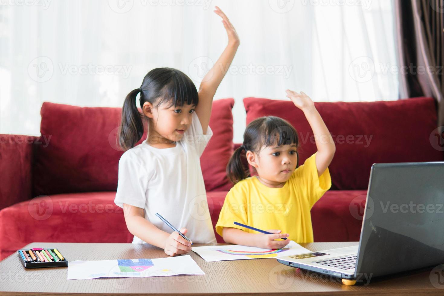 Two asian child girl students study online with teacher by video call together. Siblings are homeschooling with computer laptop during quarantine due to Covid 19 pandemic. photo