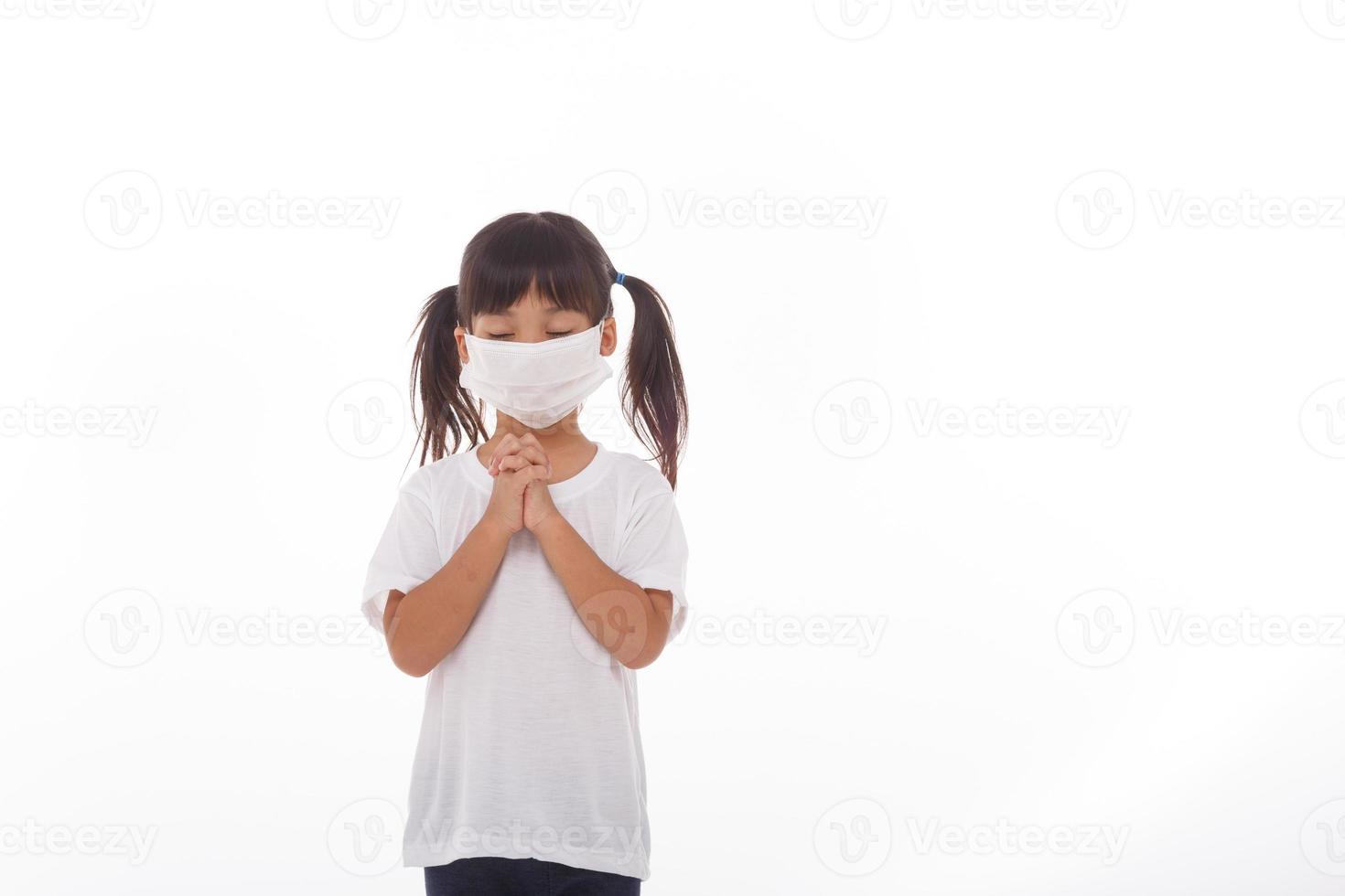 Asian girl wearing mask for protect pm2.5 and coronavirus Covid-19.Stay at home praying to GOD.Online church worship in sunday.Little asian girl hand praying at home.Social distancing. photo