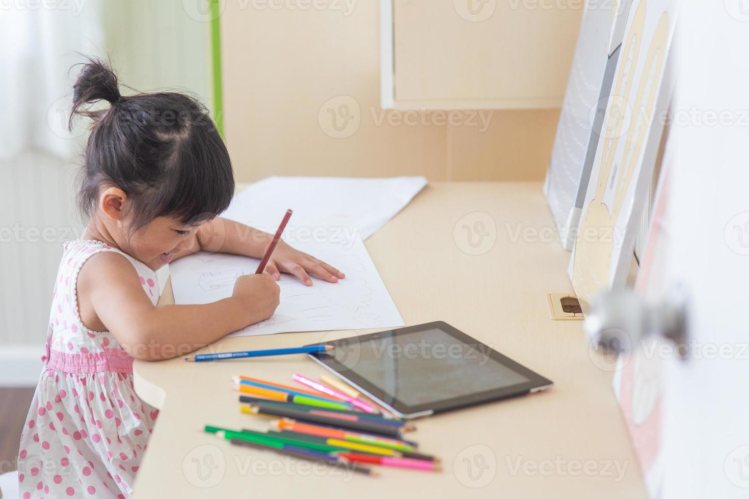 Little Asian child using a pencil to write on notebook at the desk photo