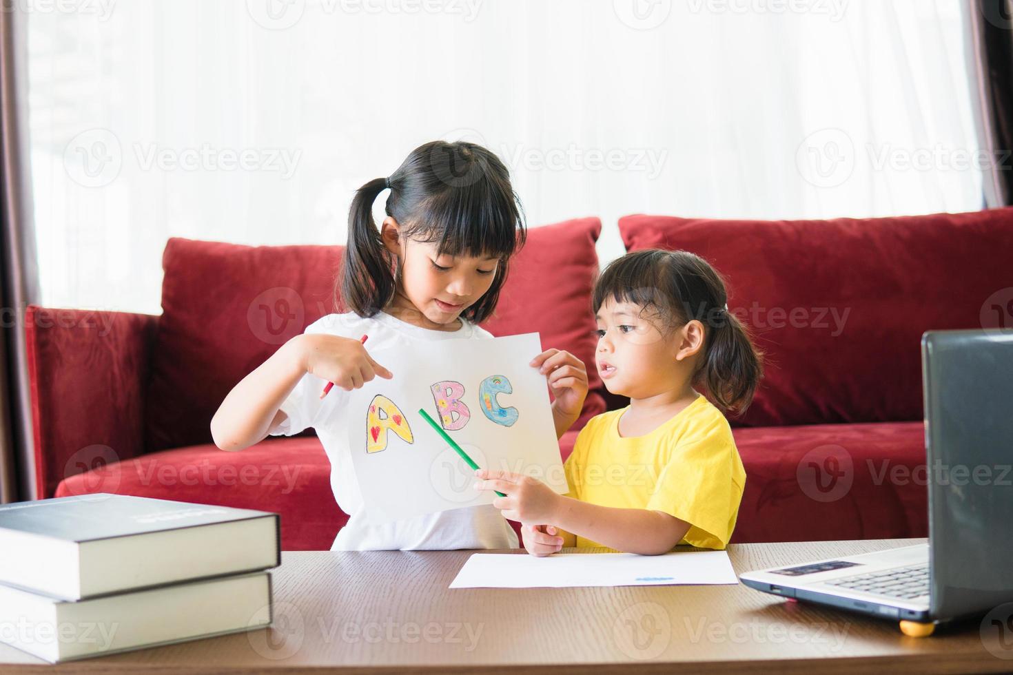 Two asian child girl students study online with teacher by video call together. Siblings are homeschooling with computer laptop during quarantine due to Covid 19 pandemic. photo