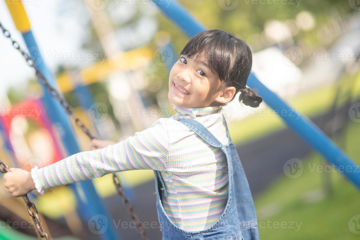 Happy little Asian girl playing swing outdoor in the park photo