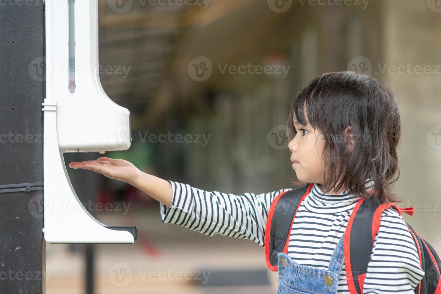 Child girls kid using automatic alcohol gel dispenser spraying on hands sanitizer machine antiseptic disinfectant, new normal life after Coronavirus COVID-19 pandemia. photo
