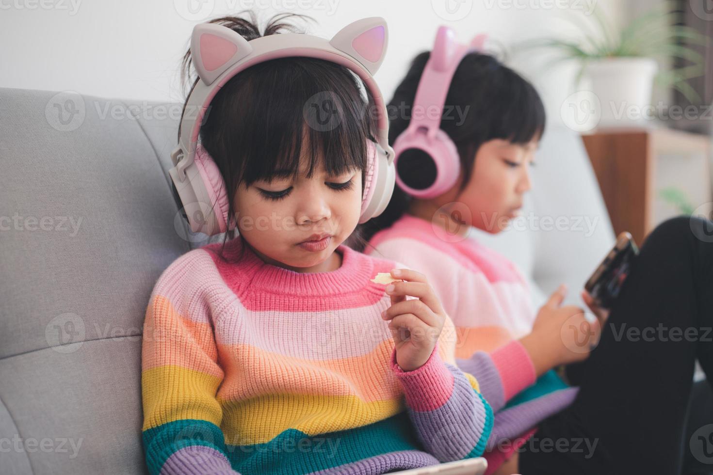 Asian siblings girl surfing net social media and playing on smartphone and digital tablet, e-learning at home photo
