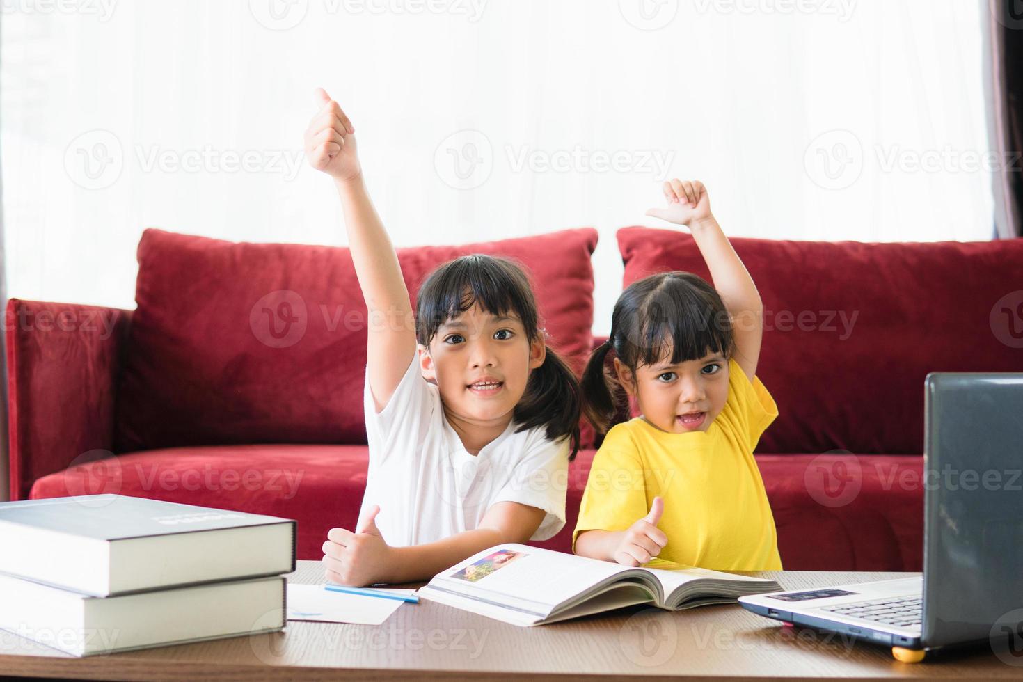 Two asian child girl students study online with teacher by video call together. Siblings are homeschooling with computer laptop during quarantine due to Covid 19 pandemic. photo