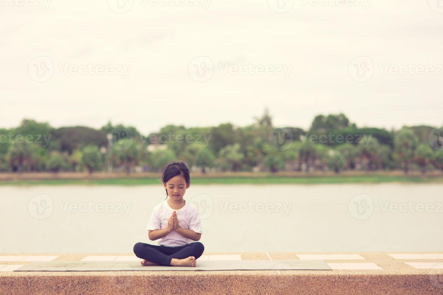 pequeña y linda niña asiática practicando pose de yoga en una alfombra en el parque, concepto saludable y de ejercicio foto