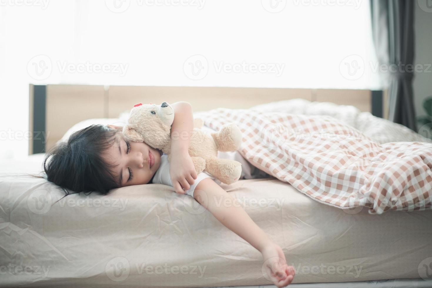 child little girl sleeps in the bed with a toy teddy bear photo