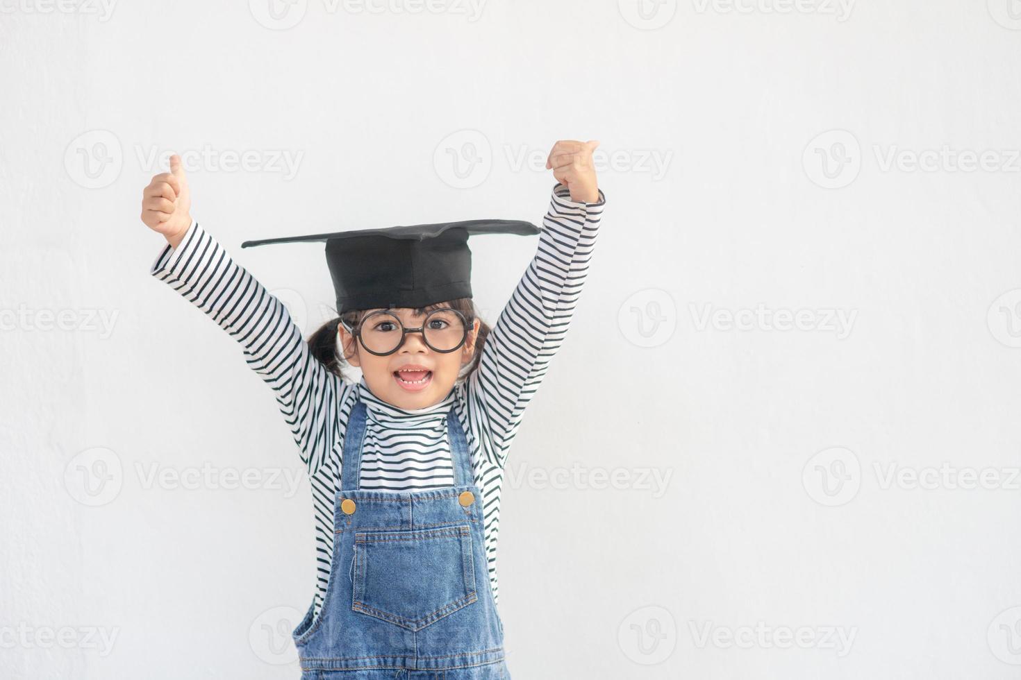 children girl wearing a graduate cap over white background very happy and excited doing winner gesture with arms raised, smiling and screaming for success. Celebration concept. photo