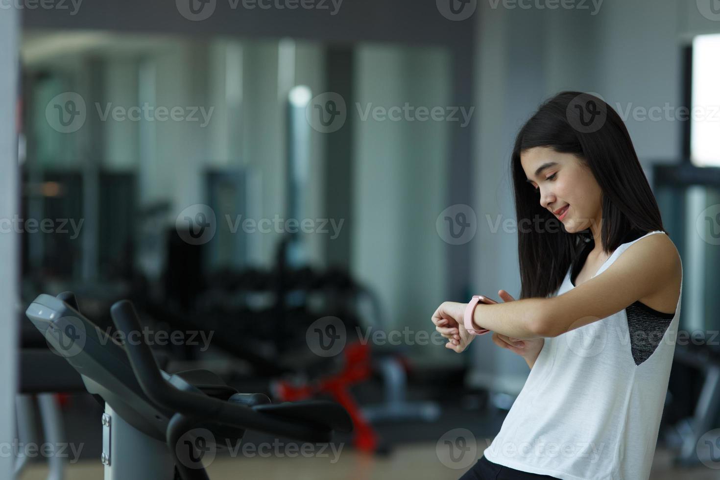 A little girl  looks at smart watch after training in gym. Healthy concept. Female after workout session checks results on watch.Children's sport concept photo