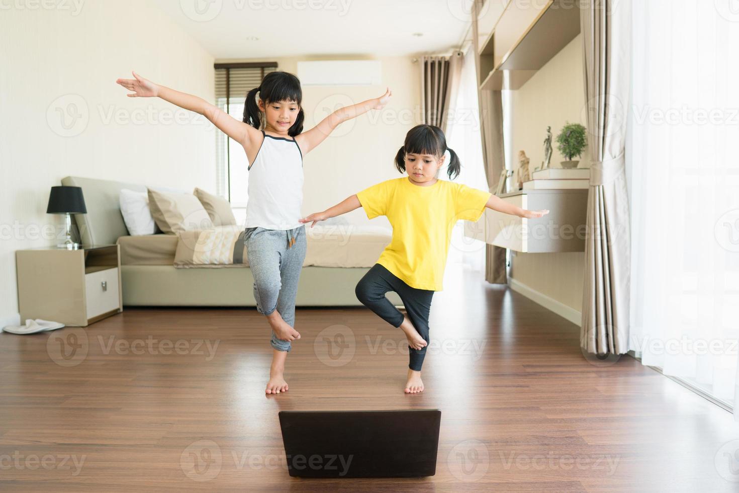 dos niñas practicando yoga, estiramientos, fitness por video en el cuaderno. entrenamiento de educación en línea distante, aeróbico en casa. estilo de vida saludable, coronavirus, quédate en casa. los niños hacen deporte en casa en cuarentena. foto