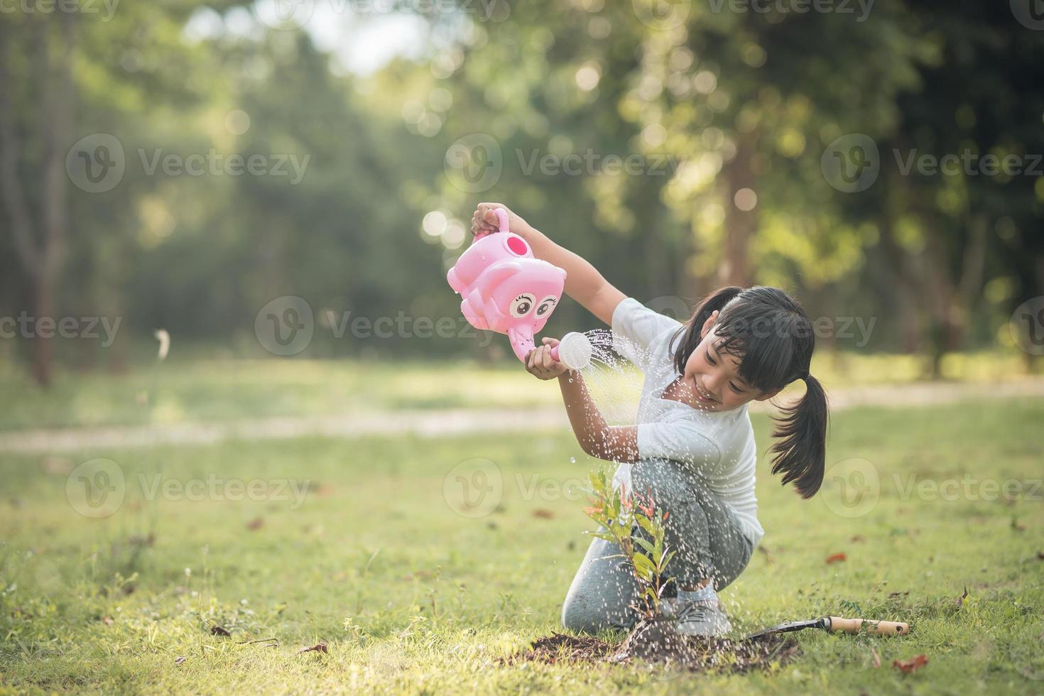 niña asiática vertiendo agua en los árboles. niño ayuda a cuidar las plantas con una regadera en el jardín. foto