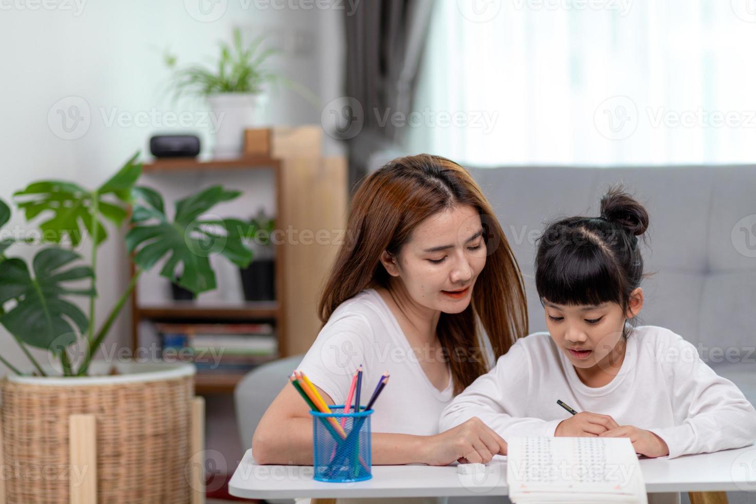 Beautiful Asian woman helping her daughter with homework at home. photo